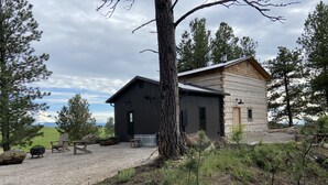 A rustic cabin with a gravel driveway, outdoor seating, and a view of the landscape. - The Log House, Montana. Handmade & luxurious cabin. 10 min from Main St.  (Lewistown)