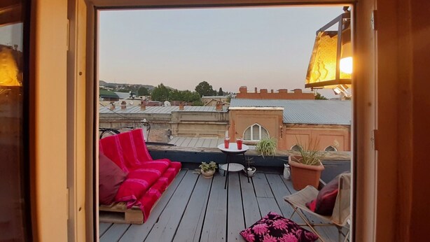 Eine Dachterrasse mit rotem Sofa, einem kleinen Tisch und Topfpflanzen.