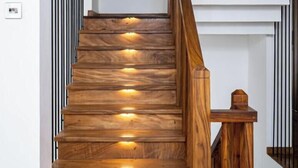 A wooden staircase with built-in lighting, a wooden handrail, and a small wooden table at the bottom.