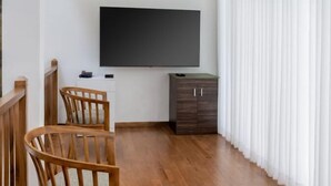 A room with a wooden floor, a TV mounted on the wall, a desk, a cabinet, and a chair.