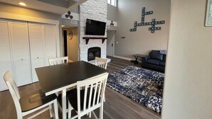 A dining area with a table and chairs, a fireplace, and a crossword puzzle on the wall. - Breathtaking Lake & Pool Views, In Osage Beach! (Osage Beach)