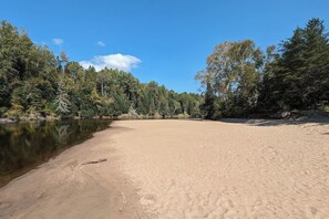 A sandy beach with a calm lake, surrounded by dense forest. - Chalet bois rond Prunier - Entièrement rénové! (Rivière-Rouge)