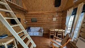 A log cabin interior with a wooden staircase, a sofa, a dining table with chairs, and a small shelf with cookware. - 4 - Prunier : Chaleureux chalet en bois rond  au bord de la belle Rivière Rouge (Rivière-Rouge)