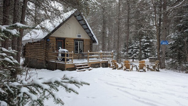 A log cabin with a wooden deck and outdoor seating. - 4 - Prunier : Chaleureux chalet en bois rond  au bord de la belle Rivière Rouge (Rivière-Rouge)