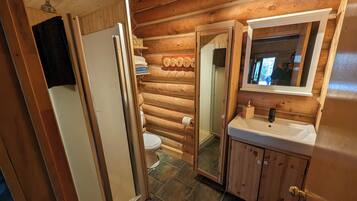 Une salle de bain rustique, aménagée dans une cabane en bois, avec des toilettes, un lavabo et une douche.