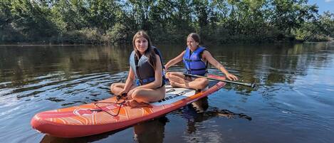 Two individuals sitting on a paddleboard in a calm body of water, surrounded by trees.