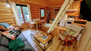 A cozy log cabin interior with a dining area, kitchen, and a staircase. - Chalet bois rond Prunier - Entièrement rénové! (Rivière-Rouge)