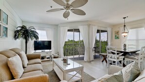 Uma sala de estar ampla com televisão de tela plana, ventilador de teto e varanda com área de jantar.