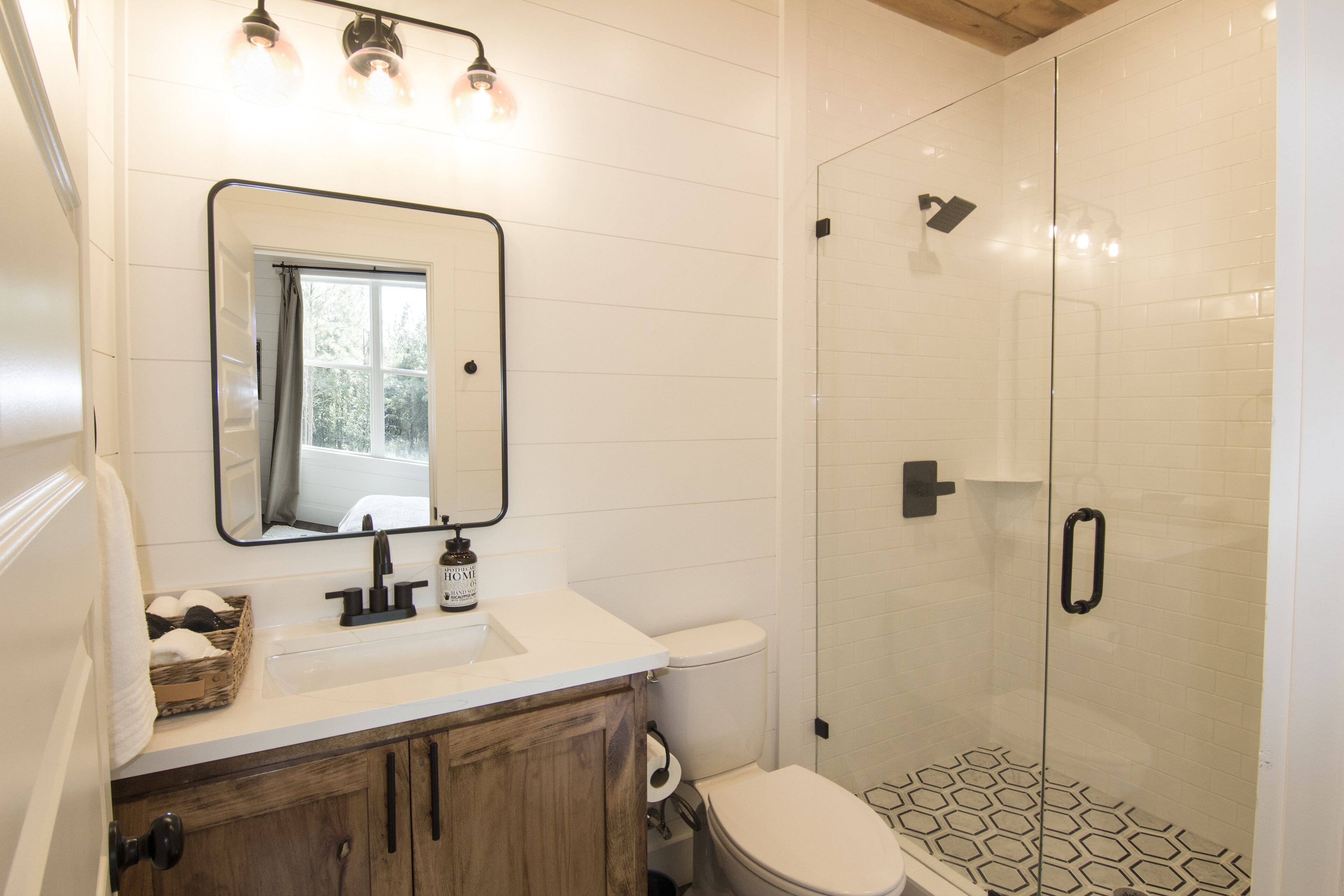 A bathroom with a white sink, wooden cabinets, a mirror, and a shower with hexagonal tiles.