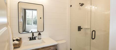 A bathroom with a white sink, wooden cabinets, a mirror, and a shower with hexagonal tiles.