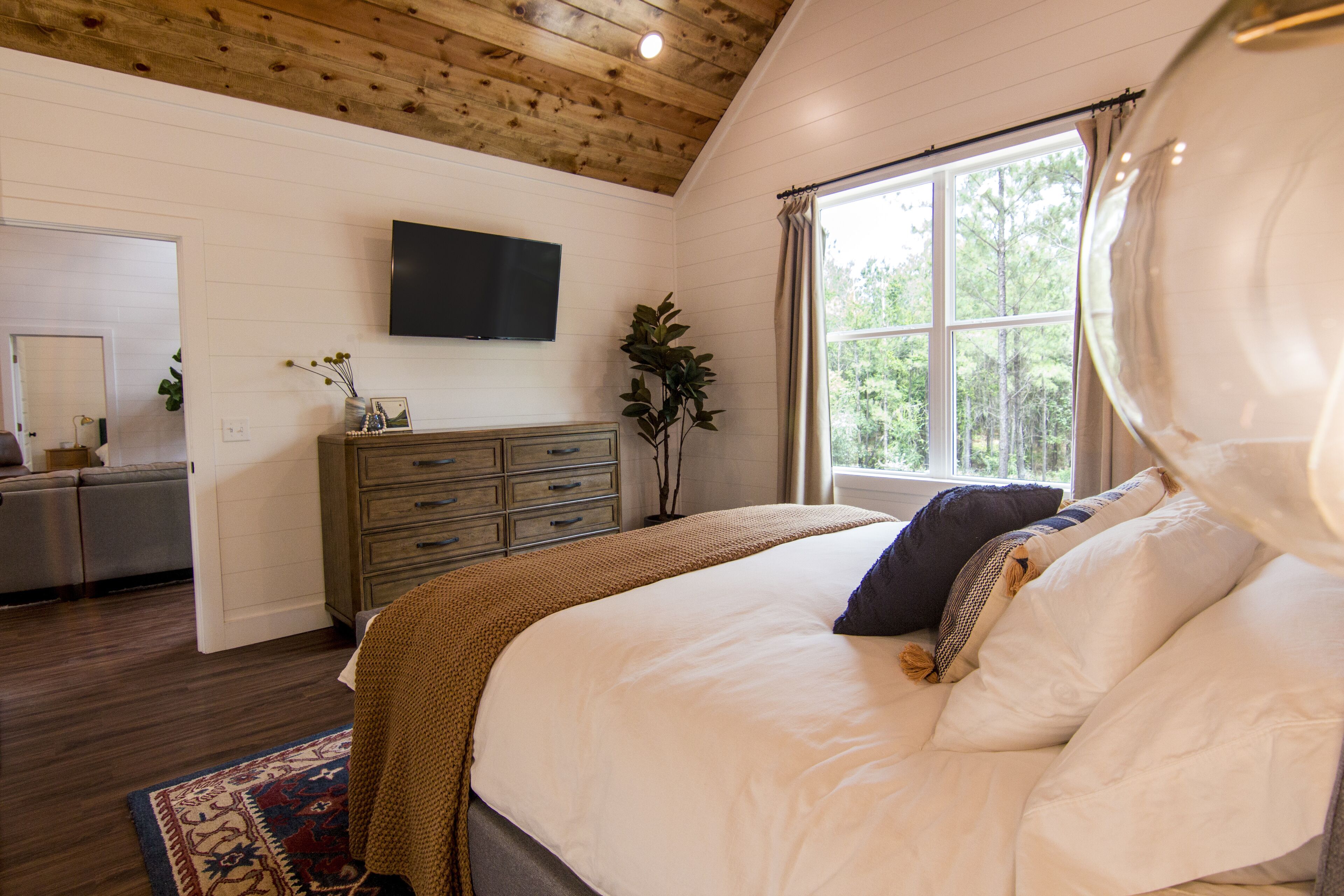 Une chambre à coucher avec un grand lit, une commode, un téléviseur à écran plat et une fenêtre avec des rideaux.