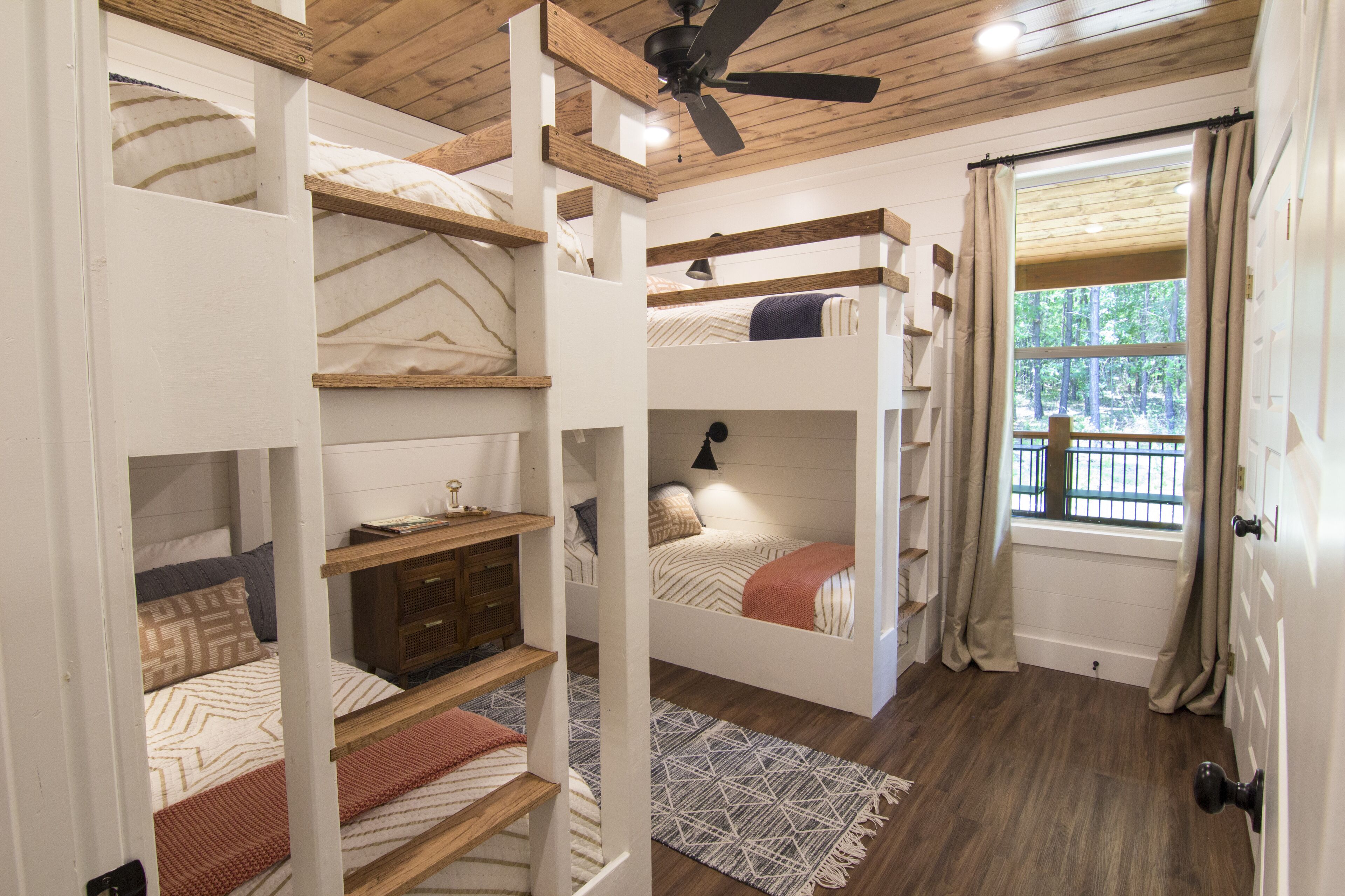 Ein Schlafzimmer mit Etagenbetten, Deckenventilator, einem Fenster mit Vorhängen und Holzboden.