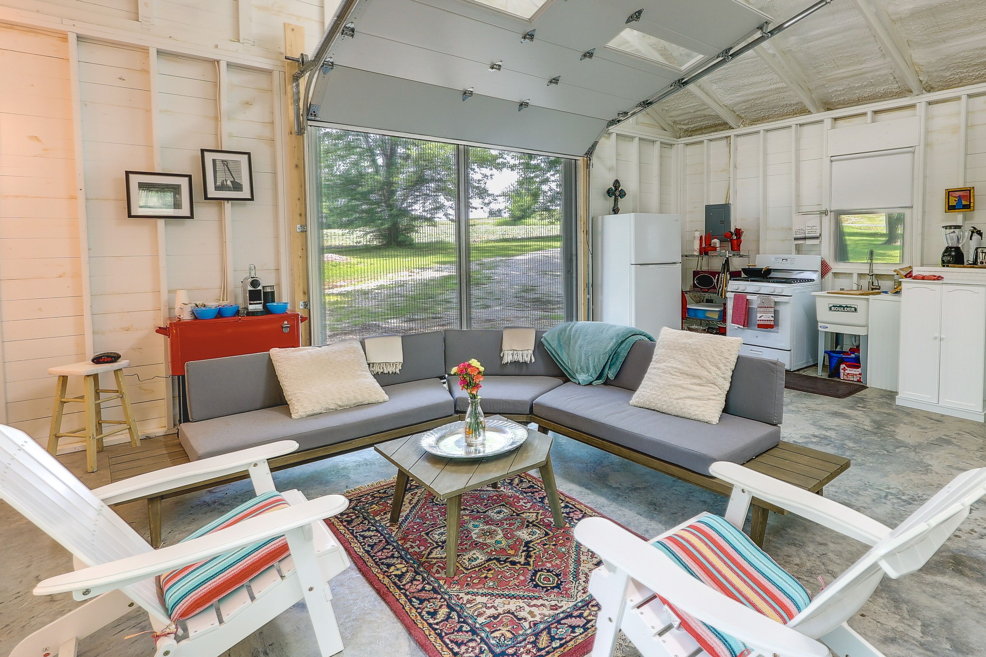 A cozy living room with a sectional sofa, two white chairs, a coffee table, and a large window offering a view of the outdoors.