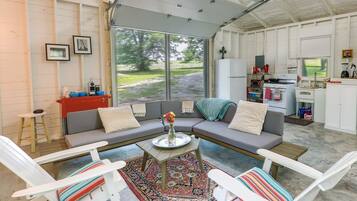 A cozy living room with a sectional sofa, two white chairs, a coffee table, and a large window offering a view of the outdoors.