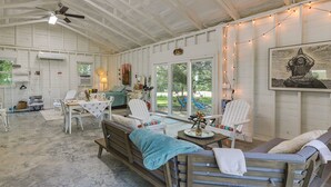 A spacious room with a high ceiling, a ceiling fan, a dining table with chairs, a bench, and a large window with a view of the outdoors. - Coffeyville Countryside Studio w/ Fire Pit! (Coffeyville)