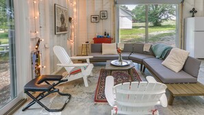 A cozy living room with a sofa, chairs, and a coffee table. There are string lights, a rug, and a window with a view of the outdoors. - Coffeyville Countryside Studio w/ Fire Pit! (Coffeyville)