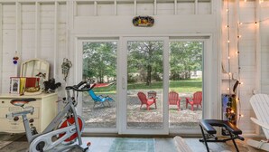 A room with a stationary bike, a desk with a mirror, and a view of a patio with outdoor chairs. - Coffeyville Countryside Studio w/ Fire Pit! (Coffeyville)