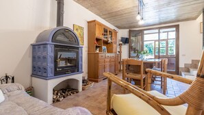 Un salon chaleureux avec un poêle à bois bleu, un buffet en bois et un coin repas avec des chaises en osier.