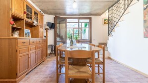 Un coin repas avec une table et des chaises en bois, un téléviseur posé sur un meuble, et un escalier doté d’une rampe en métal.