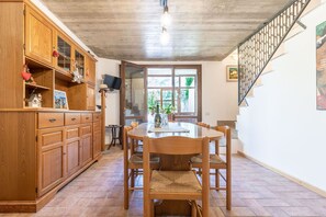Un coin repas avec une table et des chaises en bois, un téléviseur posé sur un meuble, et un escalier doté d’une rampe en métal.