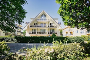 A multi-story hotel with a prominent balcony on the second floor, surrounded by lush greenery and a clear sky.