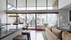 Un vaste espace de vie comprenant un grand salon avec une grande porte-fenêtre coulissante donnant sur un balcon, un canapé, une table basse et un coin repas avec un bar.