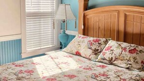 A bedroom with a floral bedspread, a wooden headboard, and a window with blinds. - Cozy 1890 Cottage Studio with Hot Tub and Fire Pit in Downtown Kennebunk (Kennebunk)