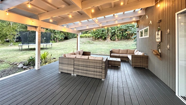 An outdoor patio with wicker furniture, a wooden deck, and a covered area with string lights.