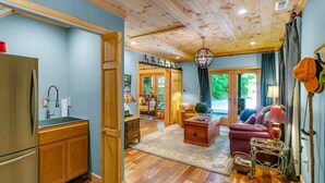 A spacious living area with a wooden ceiling, a kitchen with a refrigerator, and a dining area with a table and chairs. - KnightFall-Luxury Cabin w/Waterfall, Pet-Friendly (Maggie Valley)