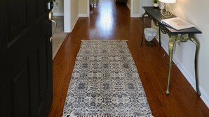 A hallway with a dark wooden door, a patterned rug, a table with a lamp, and a decorative mirror on the wall. - Cheerful Eclectic Pinehurst Home! Less than 2 miles from Pinehurst #1-4 (Pinehurst)