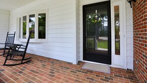 A porch with a black door, white siding, and a brick floor. - Cheerful Eclectic Pinehurst Home! Less than 2 miles from Pinehurst #1-4 (Pinehurst)