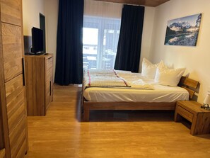 A bedroom with a bed, wooden furniture, a painting, and a window with curtains.