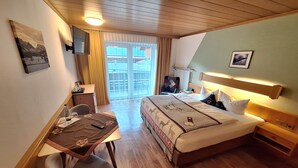 A hotel room with a bed, a desk, a chair, a TV, and a window with curtains. - Ferienwohnung mit Küche und Balkon (Reit im Winkl)
