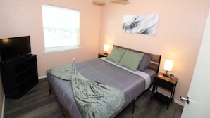 A bedroom with a bed, bedside tables, a TV, a ceiling fan, and a window. - Claremore Whole House - Just Fully Remodeled - Dogs Allowed - No Checkout Chores (Claremore)