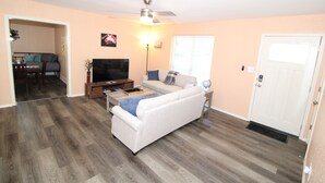 A living room with a white sofa, a coffee table, a TV, and a ceiling fan. - Claremore Whole House - Just Fully Remodeled - Dogs Allowed - No Checkout Chores (Claremore)