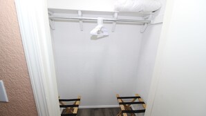 A small, narrow walk-in closet with a white door, a wooden bench, and a hanging rack with a pillow on top. - Claremore Whole House - Just Fully Remodeled - Dogs Allowed - No Checkout Chores (Claremore)