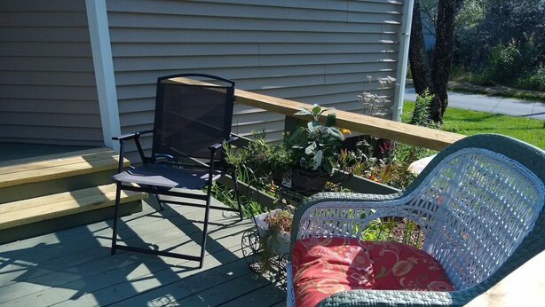 A covered outdoor area with a wooden bench, a chair, and a wicker chair. - Cozy Milbridge Country Home (Milbridge)