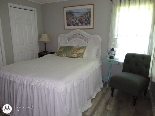 A bedroom with a bed, a nightstand, a chair, a door, and a painting on the wall.