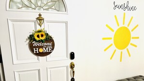 A white door with a 'Welcome to our Home' sign, a brass door knocker, and a 'Sunshine' sun decoration on the wall. - Sunshine Palace
Charming Tri-Level House with game room and large backyard! (West Chester)