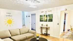 A living room with a beige sectional sofa, a round coffee table, and a white console table with two vases. There are wall art pieces depicting forests and a sun with the text "Be that ray of sunshine." - Sunshine Palace
Charming Tri-Level House with game room and large backyard! (West Chester)
