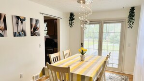 A dining area with a table set for four, a vase with yellow flowers, and a view of a garden through the glass door. - Sunshine Palace
Charming Tri-Level House with game room and large backyard! (West Chester)
