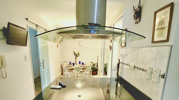 A modern kitchen with a glass cooktop, a stainless steel range hood, and a dining area with a table and chairs.