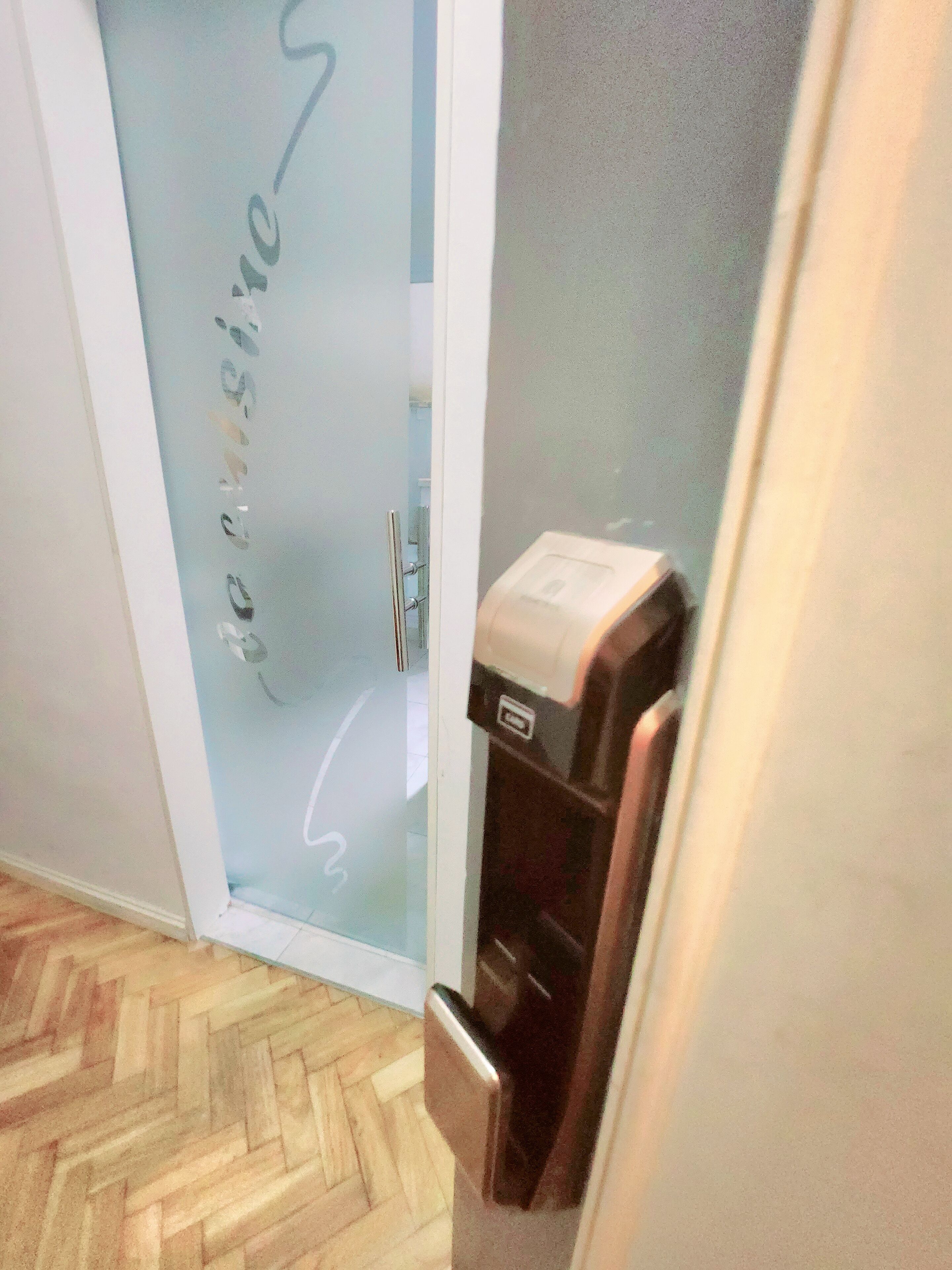 A hotel room with a wooden herringbone floor, a glass door with frosted glass, and a wall-mounted air conditioning unit.