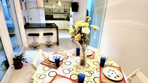 A dining area with a round table set for four, a vase with flowers, and a modern ceiling light.