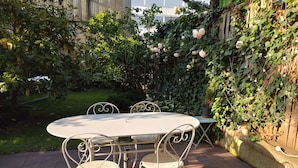 A round table with four chairs, surrounded by a garden with a wooden fence and climbing plants.