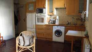 A compact kitchen with wooden cabinets, a washing machine, a microwave, and a small dining table.