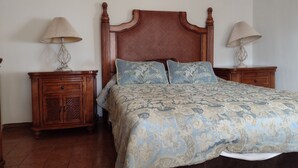 Ein Schlafzimmer mit einem Holz-Kopfteil, einer zudeckenden Bettdecke mit Blumenmuster, zwei Nachttischen mit Lampen und einem Holz-Nachttisch.