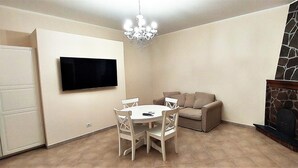 Een eetruimte met een ronde tafel en stoelen, een flatscreen televisie aan de muur, een kroonluchter, een stenen open haard en een deur.