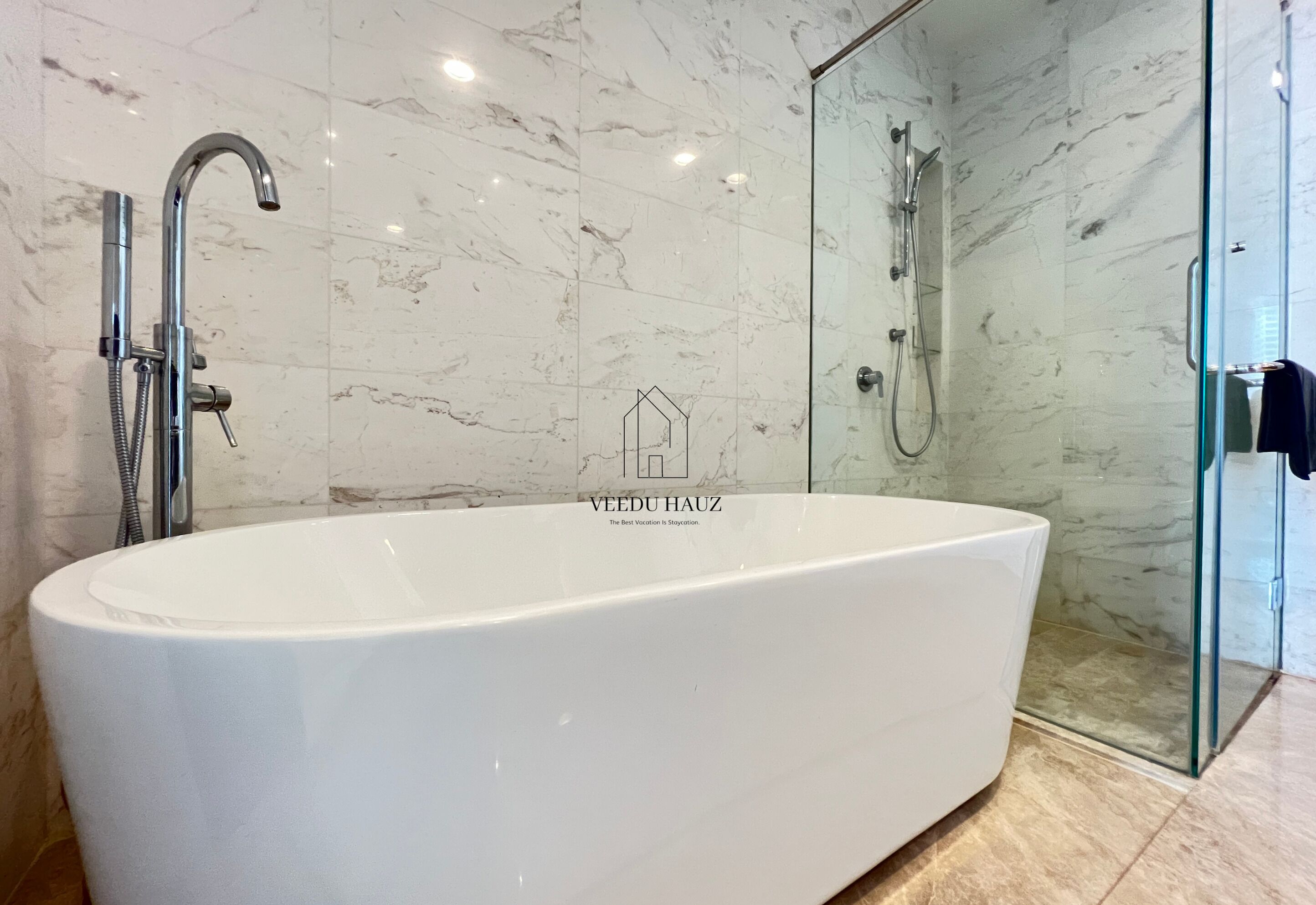 A modern bathroom with a freestanding bathtub, a glass-enclosed shower, and marble walls.
