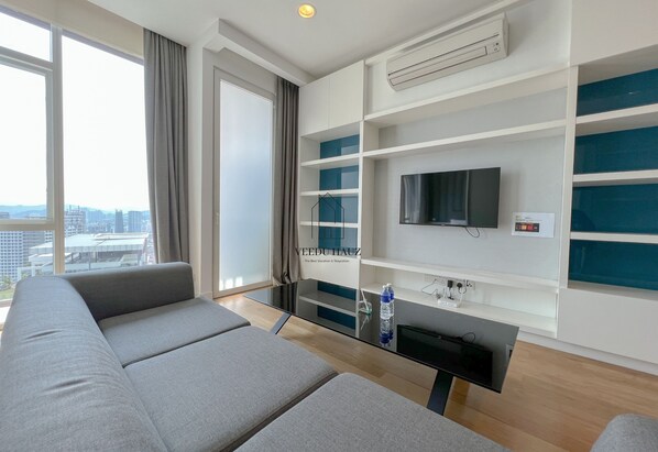 A modern living room with a sofa, a glass coffee table, a flat-screen TV, and built-in shelving. - The Platinum Suites KLCC by Veedu Hauz (Kuala Lumpur)